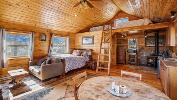 A cozy cabin with a loft bed, a dining table, a fireplace, and a kitchen area. - Phantom Canyon Resort (Victor)