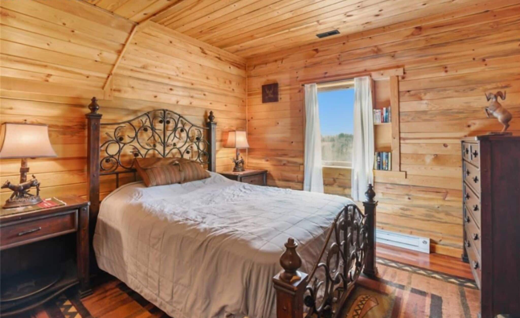 A wooden room with a bed, nightstands, a dresser, and a window.