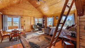 A log cabin interior with a dining area, sofa, TV, and bookshelves. - Phantom Canyon Resort (Victor)