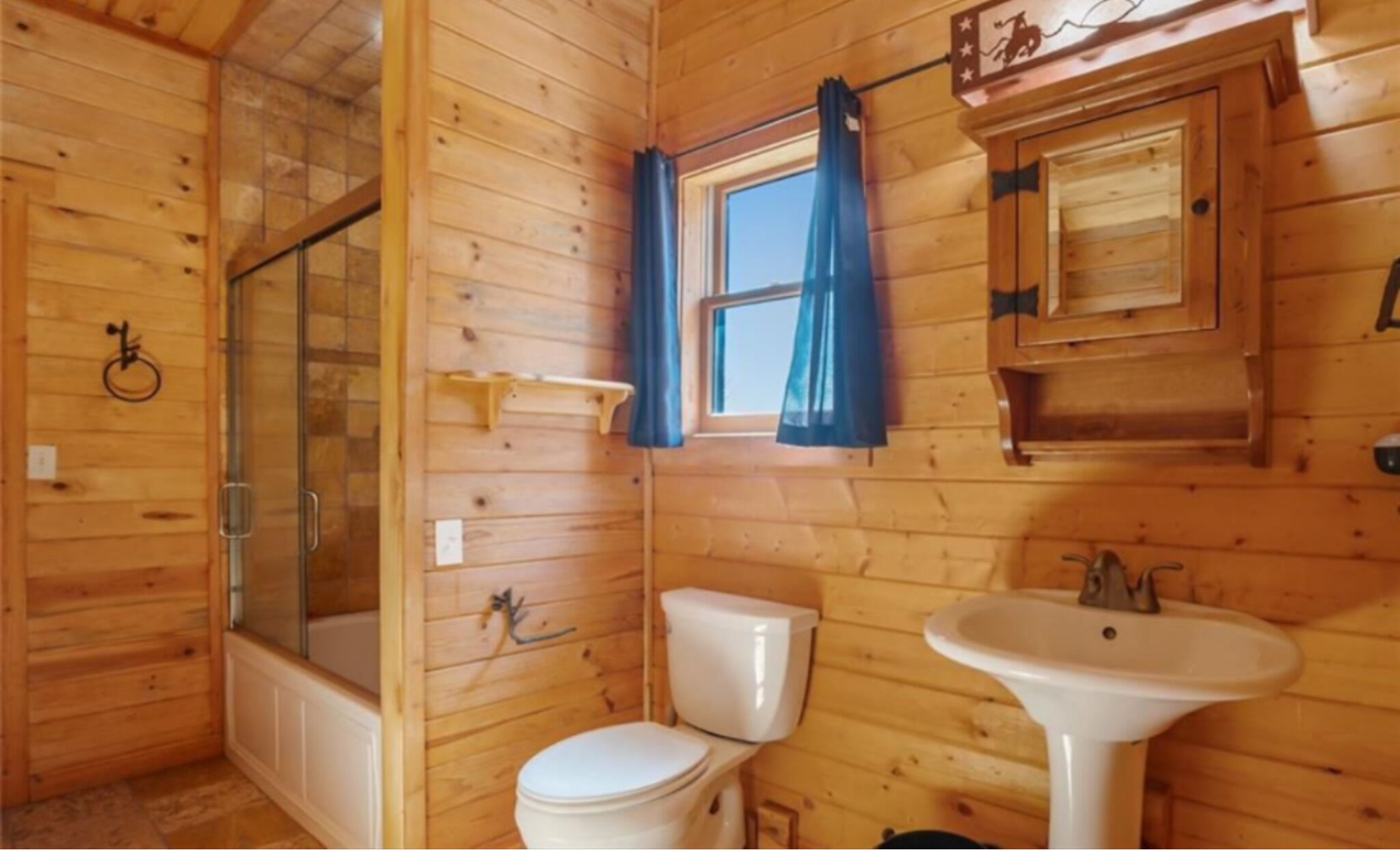 A wooden cabin bathroom with a bathtub, toilet, and sink.