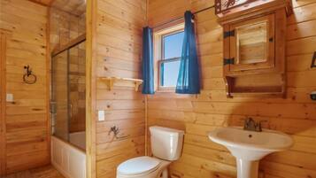 A wooden cabin bathroom with a bathtub, toilet, and sink.