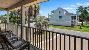 A balcony with wicker furniture, a view of a street, and a light blue house with a balcony. - Classic 4BR Cherry Grove home w/ elevator, full kitchen & short walk to beach (North Myrtle Beach)