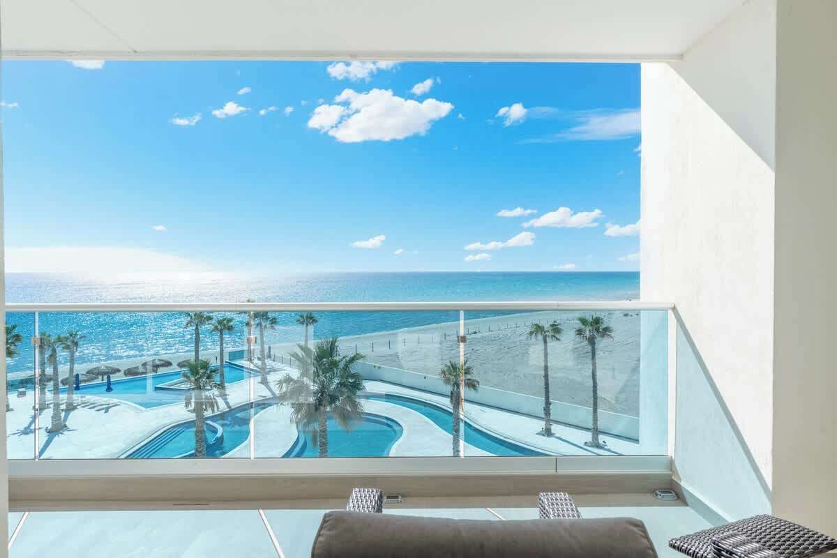 Un balcon avec vue sur une piscine, des palmiers et l’océan.