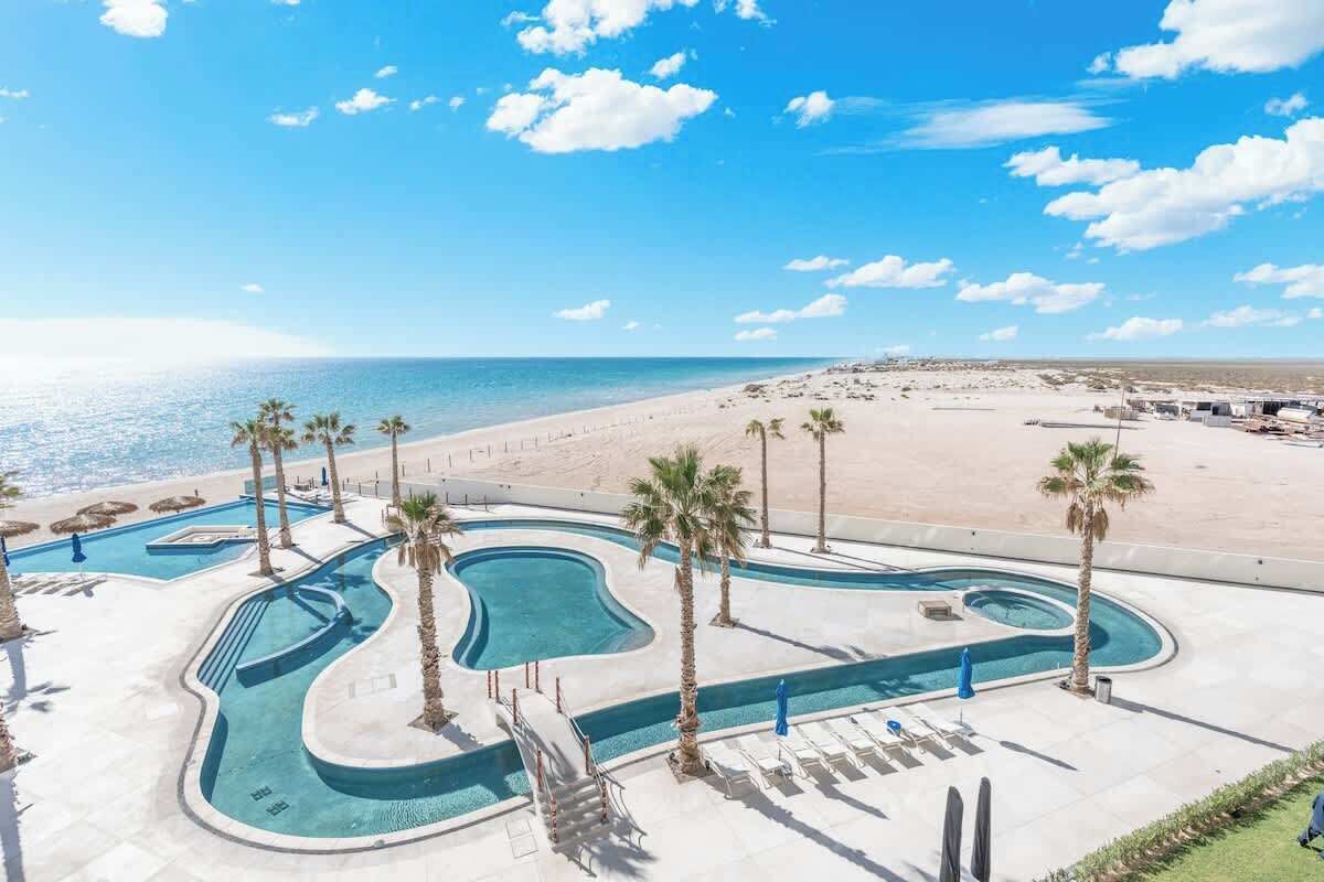 Un complexe hôtelier doté d’une piscine, de palmiers et offrant une vue sur la plage.
