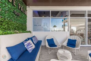 A seating area with a sofa and two chairs, a wall with greenery, and a window with a cafe sign. - Encantame 405 - 2BR Dluxe | Sleeps 6 (Playa Encanto)