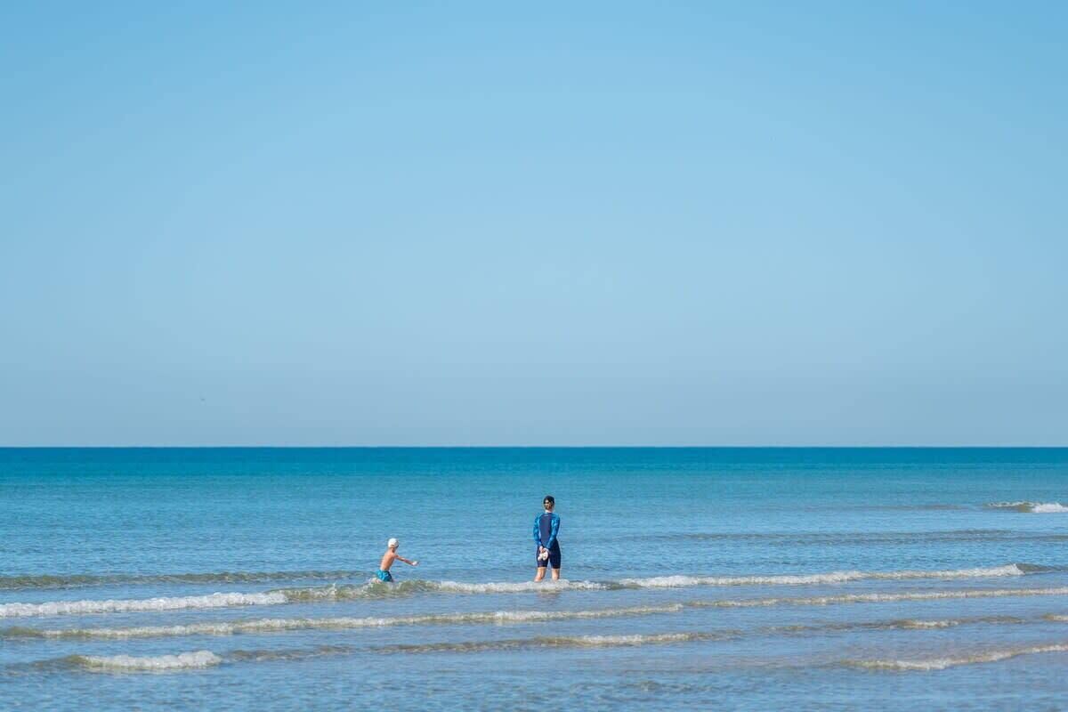 Une scène de plage où deux personnes se tiennent dans l’eau.