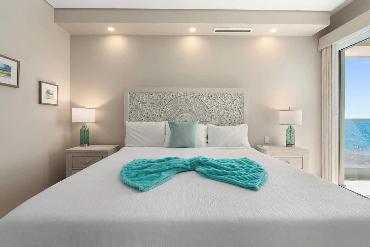 Habitación de hotel con una cama grande, dos mesitas de noche, un cabecero decorativo y vista al océano.