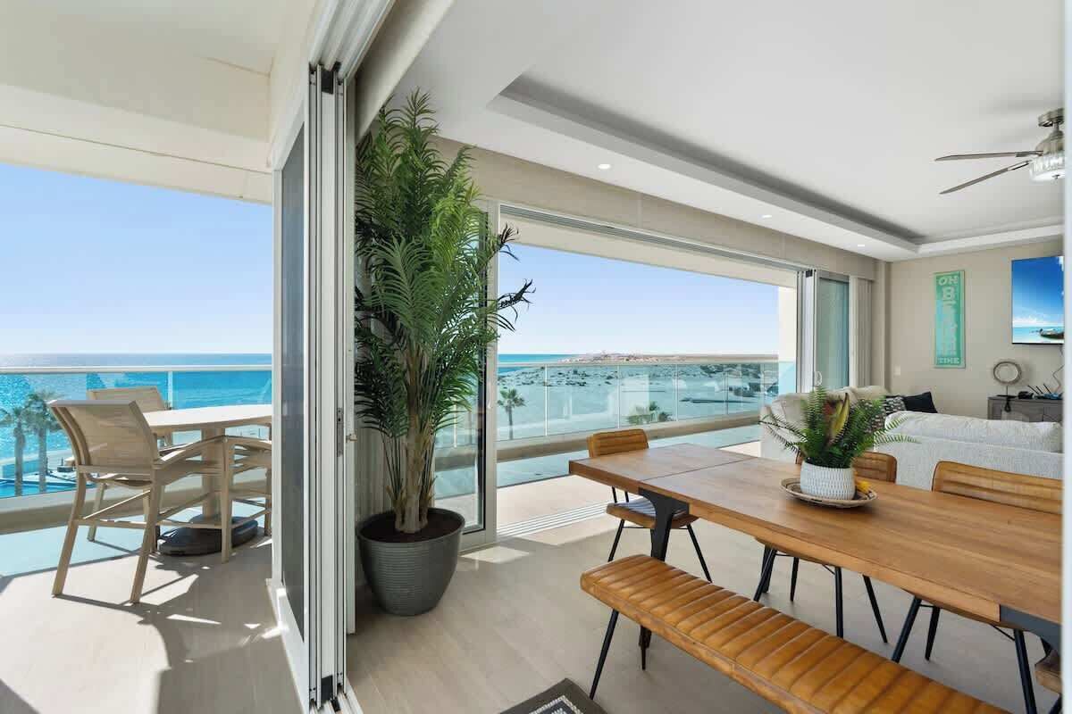 Un espace repas moderne avec vue sur la mer, une grande plante en pot et un canapé à l’arrière-plan.