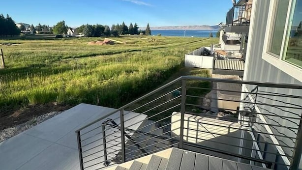A modern building with a wooden deck and a view of a green field and water. - Sleeps 30 • Hot Tub • Sauna • Pool • Walk to Bear Lake Marina (Garden City)