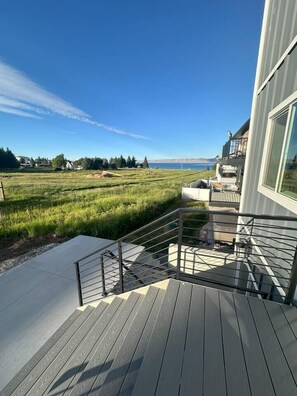 A modern building with a wooden deck and a view of a green field and water. - Sleeps 30 • Hot Tub • Sauna • Pool • Walk to Bear Lake Marina (Garden City)