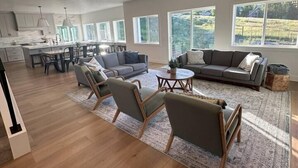 A spacious living area with a large sofa, armchairs, and a coffee table. There is a kitchen in the background with a dining area. - Sleeps 30 • Hot Tub • Sauna • Pool • Walk to Bear Lake Marina (Garden City)