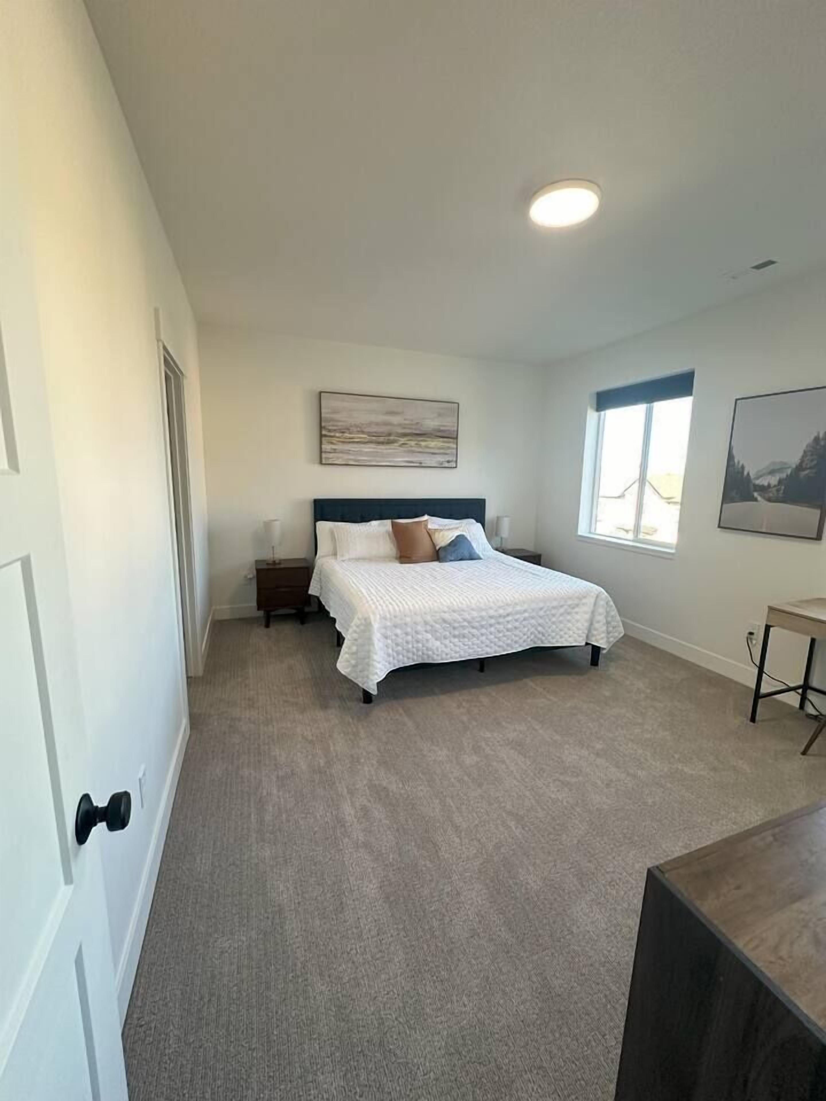 A bedroom with a bed, a nightstand, a window, and a painting on the wall.