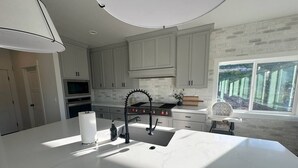 A modern kitchen with a large island, white cabinetry, and a view of the outdoors. - Sleeps 30 • Hot Tub • Sauna • Pool • Walk to Bear Lake Marina (Garden City)