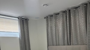 A neatly made bed with a white comforter and pillows, a headboard, and a window with blinds. - Restful Haven (Winnipeg)
