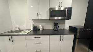 A modern kitchen with white cabinets, a stainless steel microwave, a coffee maker, and a black refrigerator. - Restful Haven (Winnipeg)