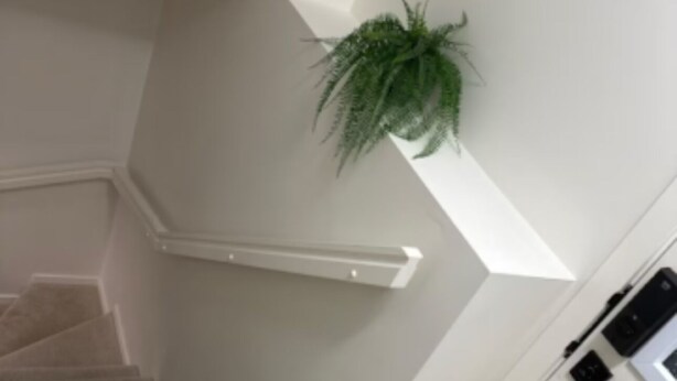 A staircase with a light wood finish, white walls, and a small green plant on the wall. - Restful Haven (Winnipeg)