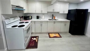 Une cuisine moderne avec des meubles blancs, un réfrigérateur noir, une cuisinière et un four à micro-ondes.
