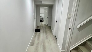 Un couloir doté d’un parquet en bois clair, de murs blancs et d’un paillasson noir au pied d’un escalier.