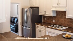 Una cocina con gabinetes blancos, un refrigerador de acero inoxidable, una estufa a gas y una encimera de granito.