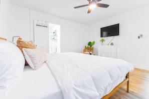 Une chambre à coucher comprenant un lit, un ventilateur de plafond, un téléviseur et un meuble de rangement.