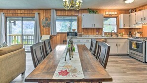 A spacious kitchen with wooden cabinets, a dining area with a large table, and a chandelier. - Crystalwood-Cozy Cabin w/Views+Creek, Easy Access! (Maggie Valley)