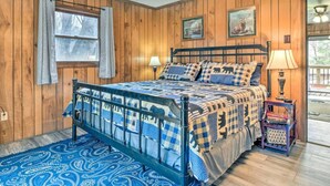 A bedroom with a wooden paneled wall, a bed with a blue and white checkered bedspread, a ceiling fan, and a window with curtains. - Crystalwood-Cozy Cabin w/Views+Creek, Easy Access! (Maggie Valley)