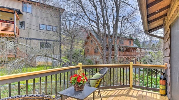 A wooden deck with a table and chairs, a wicker basket with flowers, and a bottle on the railing. - Crystalwood-Cozy Cabin w/Views+Creek, Easy Access! (Maggie Valley)