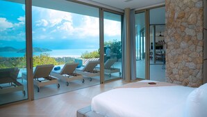 A bedroom with a large bed, a stone accent wall, and a view of the sea through floor-to-ceiling glass doors. - Villa Akoya by Sublime Samui Villas (Koh Samui)