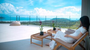 A balcony with a view of the sea and mountains, a wooden table, a chair, and a potted plant. - Villa Akoya by Sublime Samui Villas (Koh Samui)