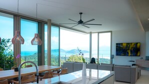 A modern kitchen with a large island, a dining area, and a view of the mountains. - Villa Akoya by Sublime Samui Villas (Koh Samui)