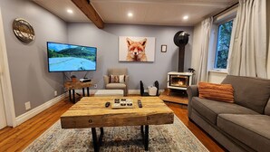 A cozy living room with a wooden coffee table, a grey sofa, a fireplace, a television, and a painting of a fox. - L'Ancestrale (view, spa, arcade) (La Malbaie)