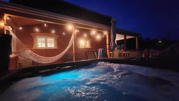 A heated outdoor pool with a hammock, a covered patio, and a house with string lights. - L'Ancestrale (view, spa, arcade) (La Malbaie)