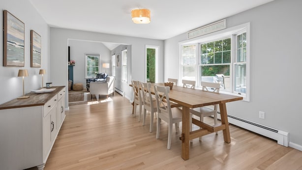 Un vaste espace dédié à la salle à manger, avec une table et des chaises en bois, de grandes fenêtres et une vue sur la verdure environnante.