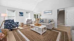 Un salon spacieux avec un plafond haut, un canapé blanc, un fauteuil gris et une table basse.