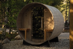 A wooden cylindrical structure with a door, benches, and a stand.