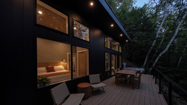 A modern house with a deck, large windows, and a cozy interior with a bed and seating area. - Luxe Cozy Spa Cabin w/ Hot Tub, Sauna, Fireplace, 10 mins to Sunday River (Newry)