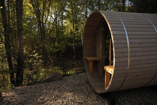 A wooden cylindrical structure with a bench inside, surrounded by a forest.