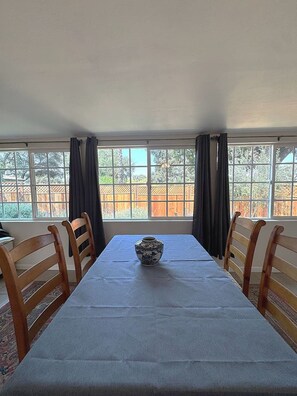 A dining area with a table set for four, a vase on the table, and a view of a wooden fence and trees outside.