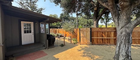 A residential property with a covered porch, a barbecue grill, a fenced backyard, and a large tree.