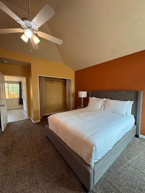 A hotel room with a large bed, a ceiling fan, a nightstand with a lamp, and a wardrobe.