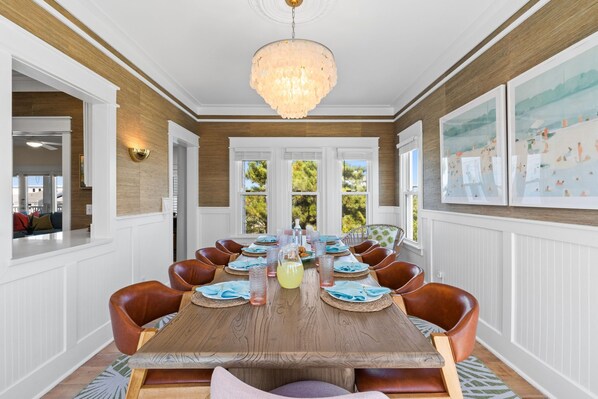 A dining room with a long wooden table, brown leather chairs, and a chandelier.