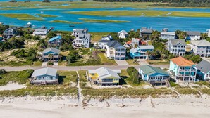Vue aérienne d’un quartier résidentiel situé sur la côte, avec des maisons près d’une plage et d’une vaste étendue d’eau.