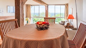 A round table with a woven tablecloth, a basket of fruit, and a view of the outdoors through large windows. - La Pinchonnière by Interhome (Deauville-Trouville)