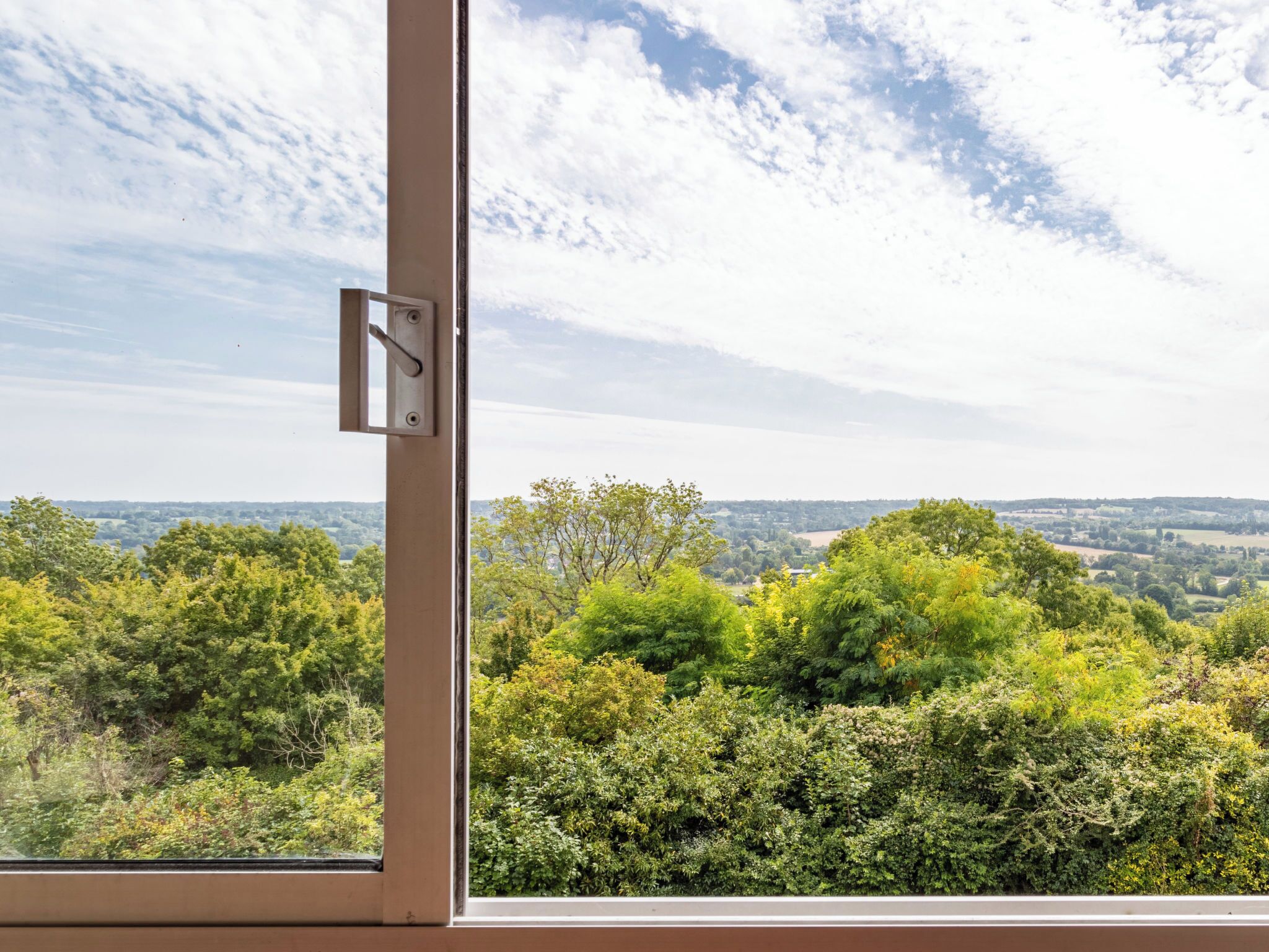 A window with a view of a green landscape and a partly cloudy sky.