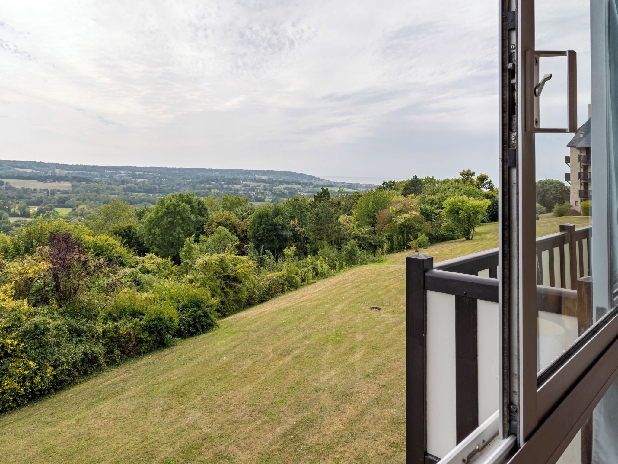 A balcony with a view of a grassy hill and trees.