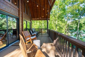 A wooden deck with outdoor seating, large windows, and a view of a forest.