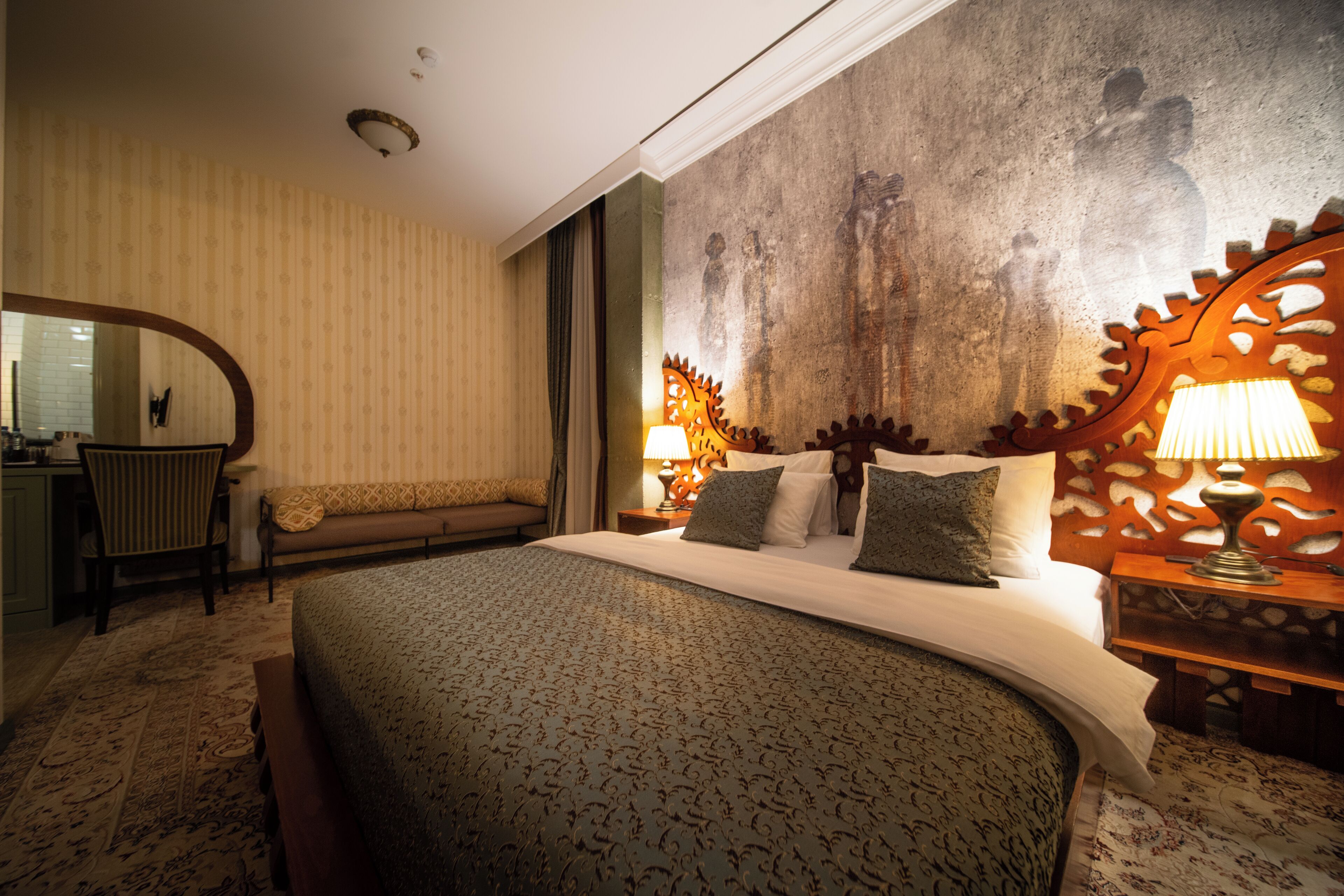 A hotel room with a large bed, a desk, a chair, and a patterned carpet.