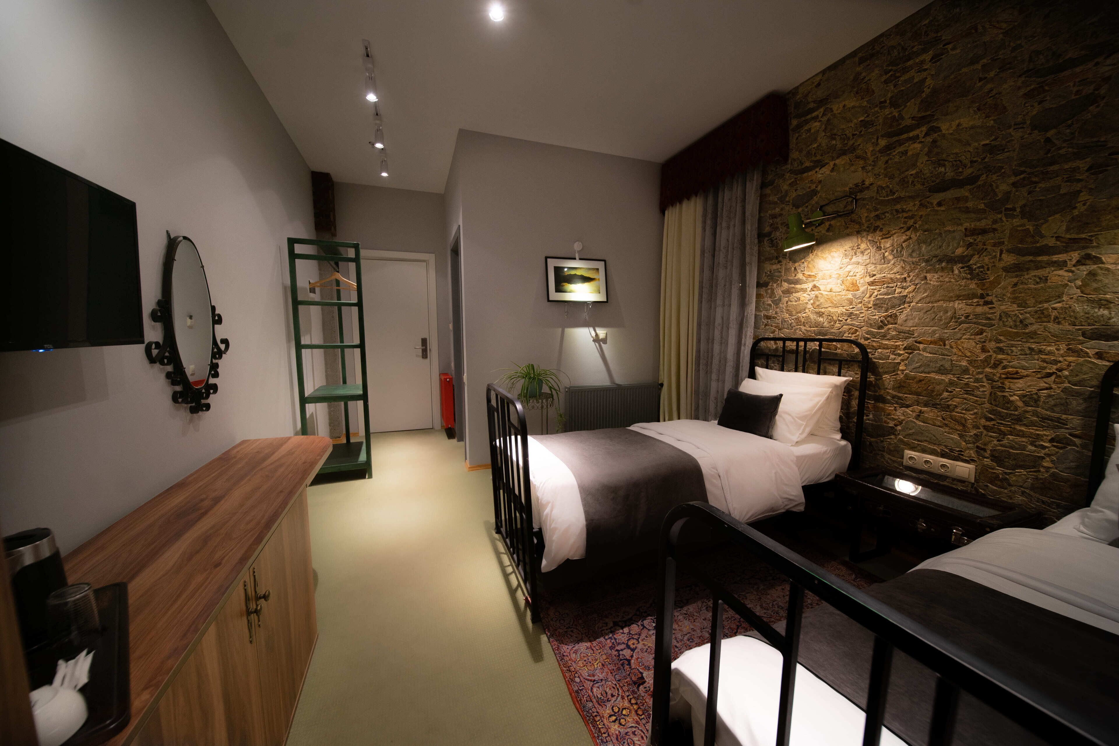 A hotel room with a bed, bedside table, dresser, and a stone accent wall.