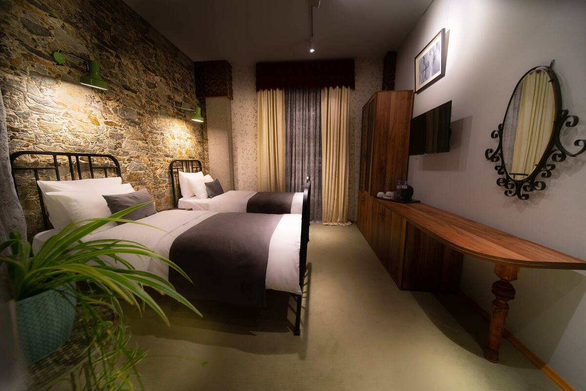Un dormitorio con dos camas, un escritorio de madera, un espejo y una pared de piedra.