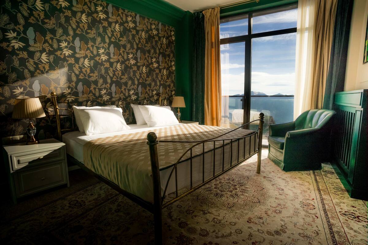 Un dormitorio con cama, mesitas de noche, una silla y vista al mar.